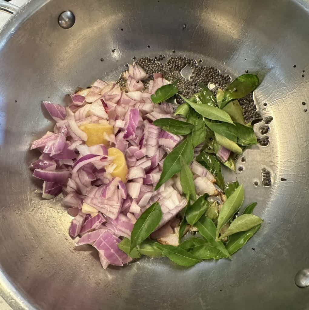 addingchopped onions, ginger, and curry leaves with mustard seeds in a deep non-stick pan.