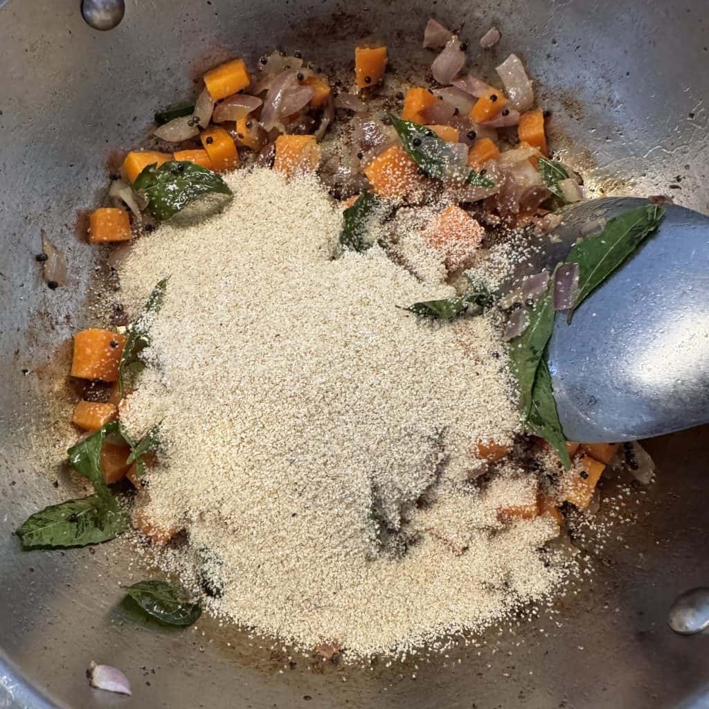 Jowar rava added to sautéed vegetables in a deep non-stick pan for roasting.