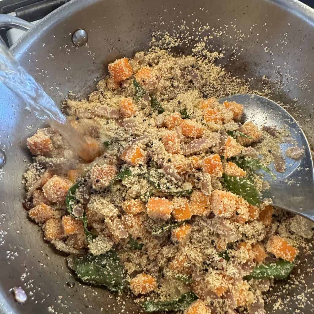 Water being poured into roasted jowar rava and vegetables in a pan.