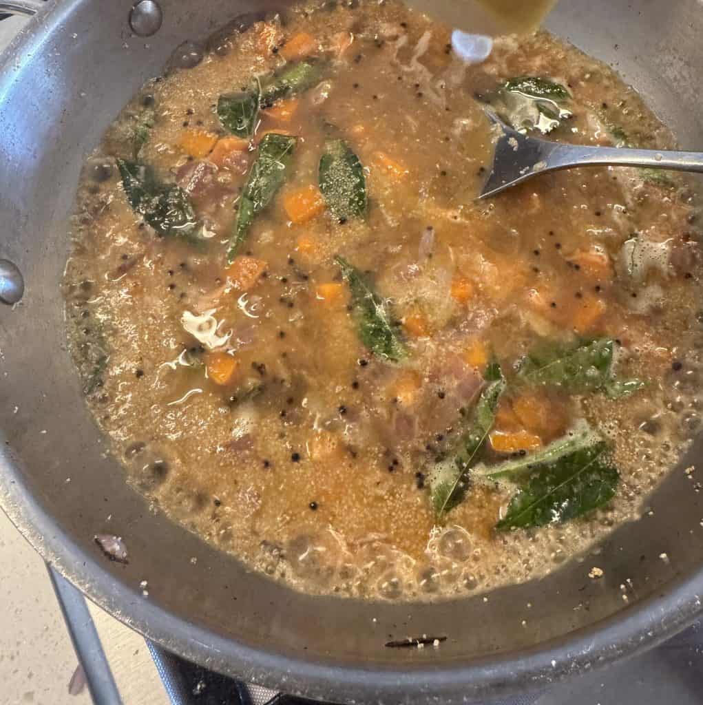 owar rava upma cooking and thickening with water, carrots, and curry leaves in a non-stick pan.