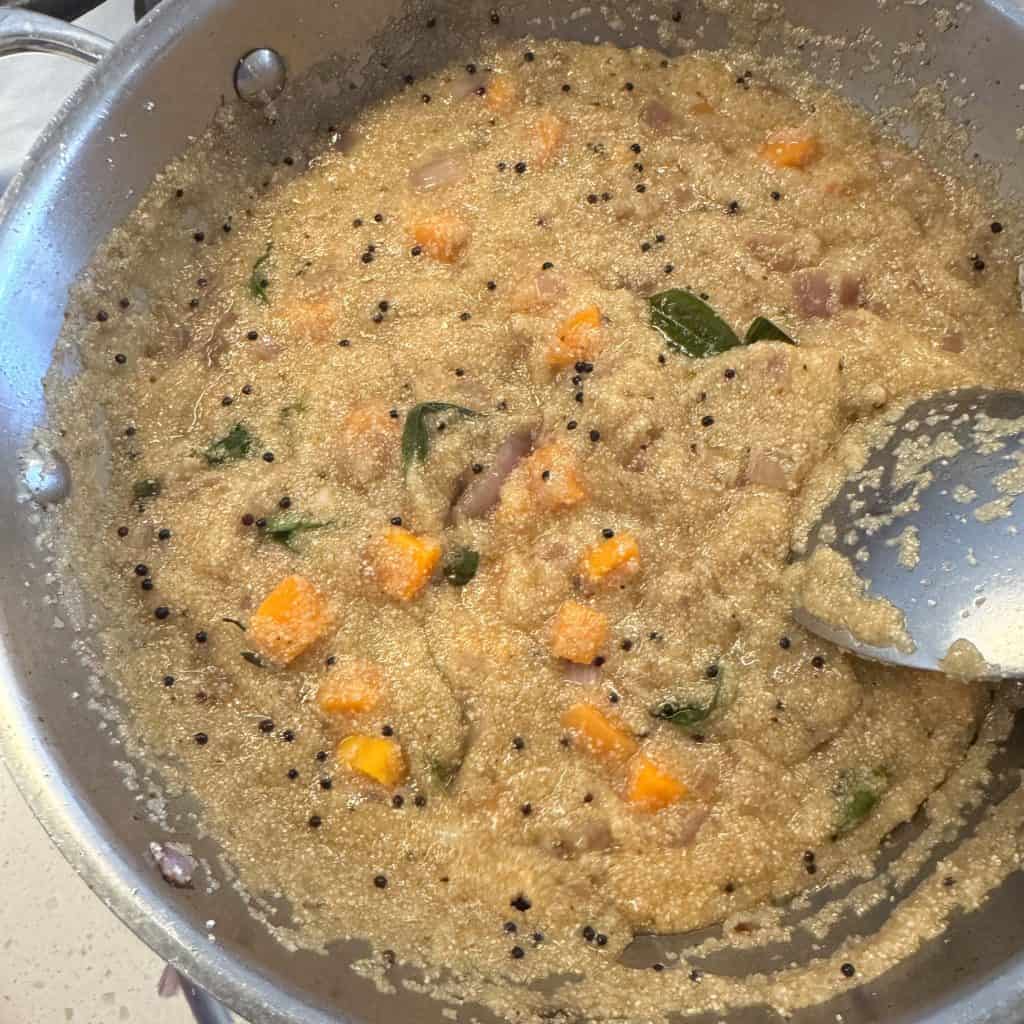Lemon juice being added to simmering Jowar Rava Upma with visible carrots and curry leaves